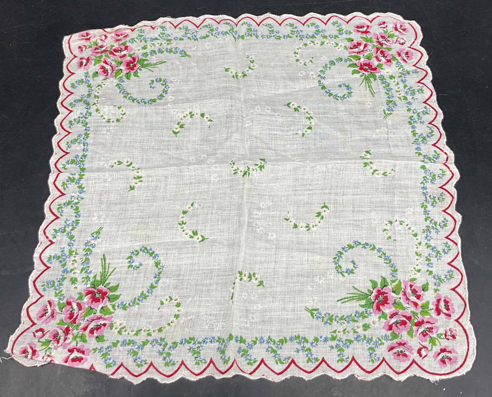 Vintage Scalloped Floral Linen Napkin: Vintage scalloped floral linen napkin. Scalloped trim. Red scalloped border. Floral motifs in green, pink, blue, yellow, white. Measures approx 13 x 13 inches. Surface wear consistent with exposure. N