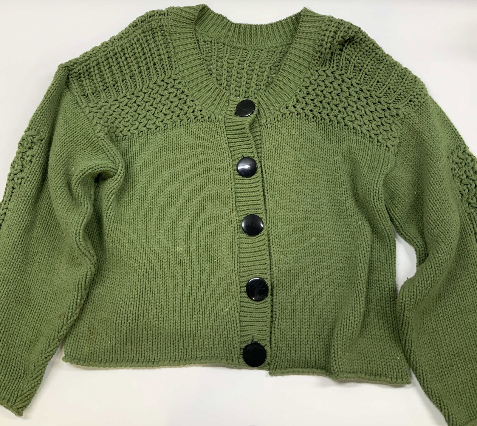 Crewneck knit cropped cardigan: Crewneck knit cropped cardigan. Using a green moss shade yarn. It features a chunky, heavyweight construction, drop shoulders and a unique textured knit pattern across the chest, shoulders, and elbows