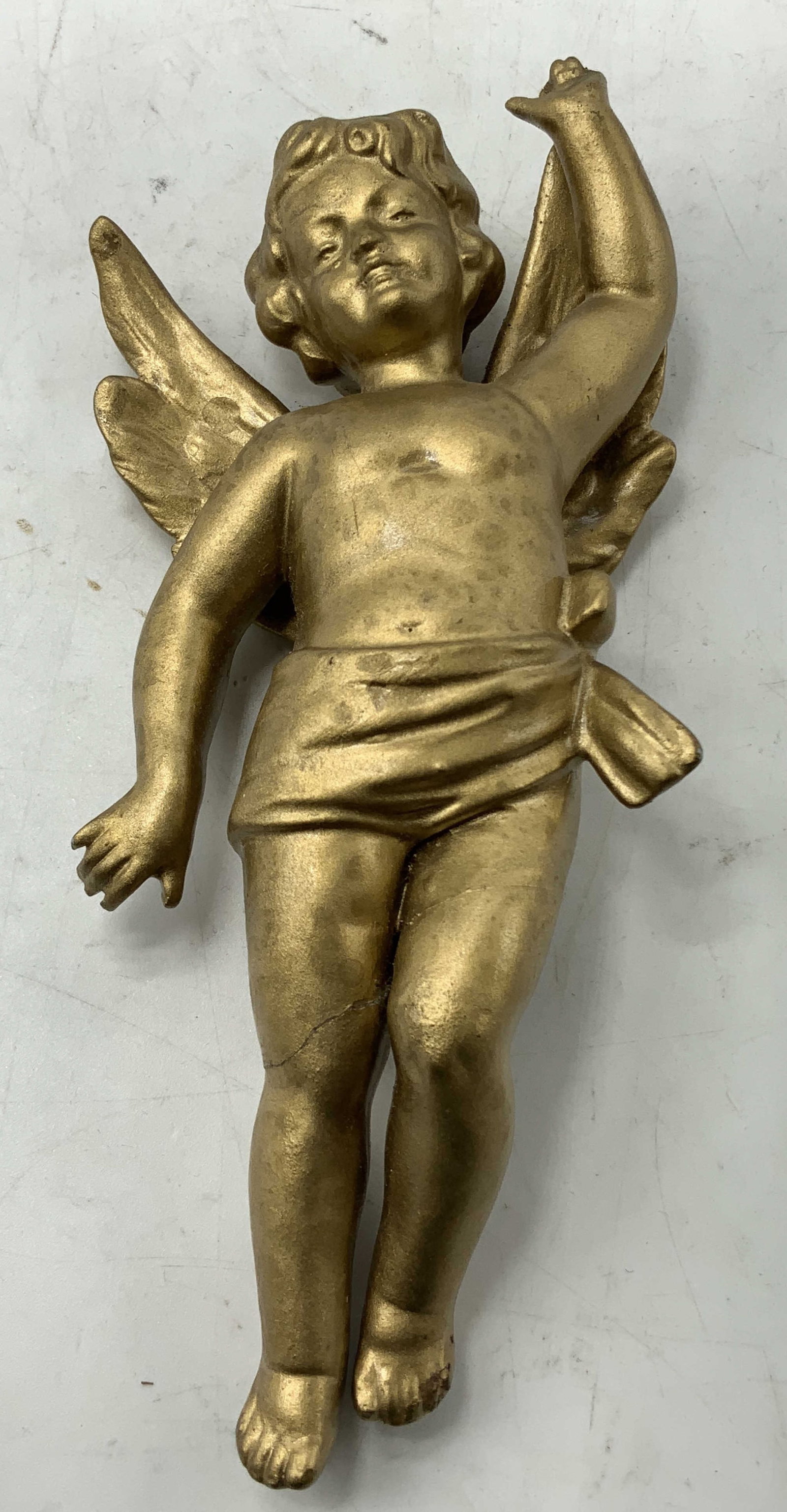 Vtg Gilt Porc Cherub Hanging Wall Decor: Vintage cherub is depicted w one arm raised upwards. Porcelain material w a gilt finish. Surface wear consistent to age, use & exposure. Visible cracking on leg & chipping. No visible signature or mar