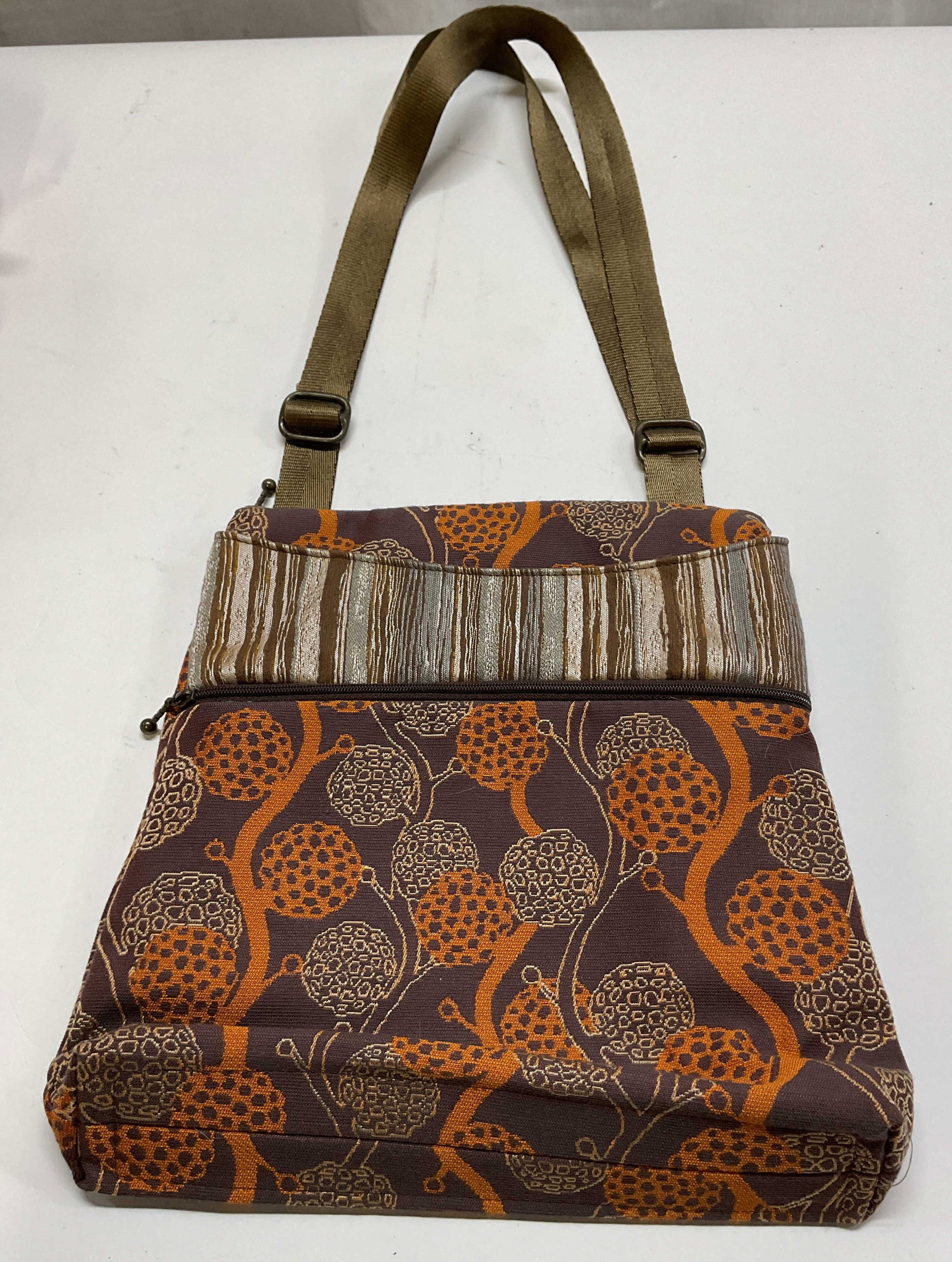 Maruca Design Spree Crossbody Bag USA: Maruca Design spree crossbody bag. Handmade in Boulder Colorado. Woven fabric. Orange and brown floral and striped jacquard pattern. Adjustable olive green strap. Zippers and interior compartments.