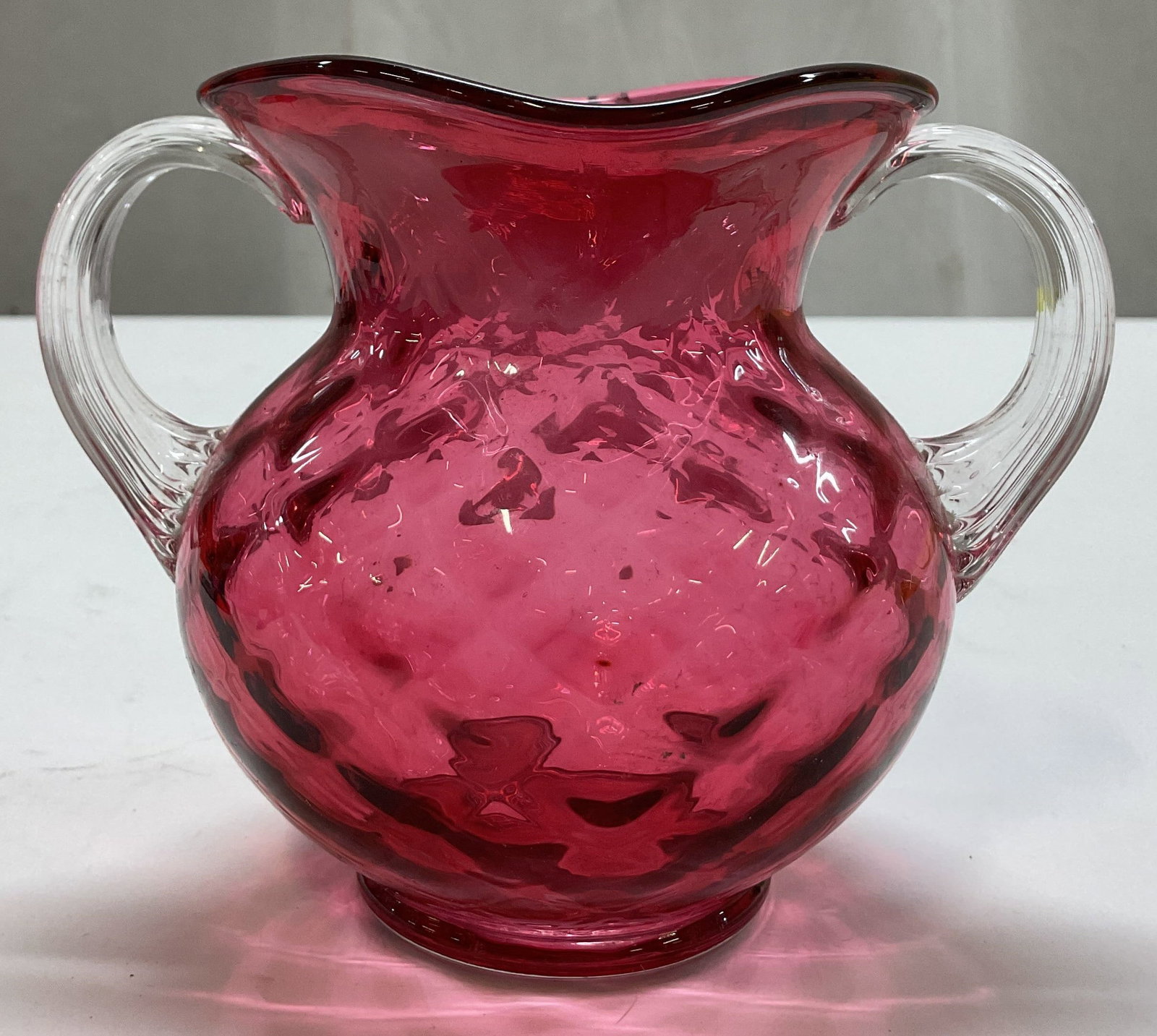Vtg Cranberry Art Glass Double Handled Vase: Vintage cranberry art glass double handled vase. Bulbous body with patterned surface. Double clear applied handles, ribbed surface. Flared rim. Measures ht approx 4.5 inches diam approx 4 inches. Scra