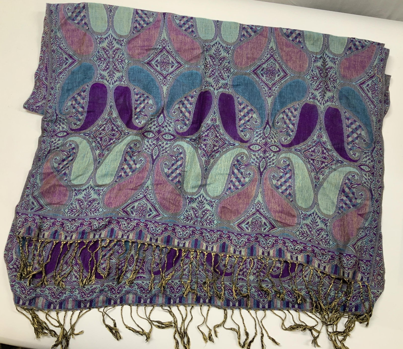 Paisley pashmina in blue, pink, and purple: Paisley pashmina in blue, pink, and purple. Made of an acrylic viscose blend fabric. It features a jacquard woven paisley motif. Woven using a double layered jacquard making the scarf reversible with 