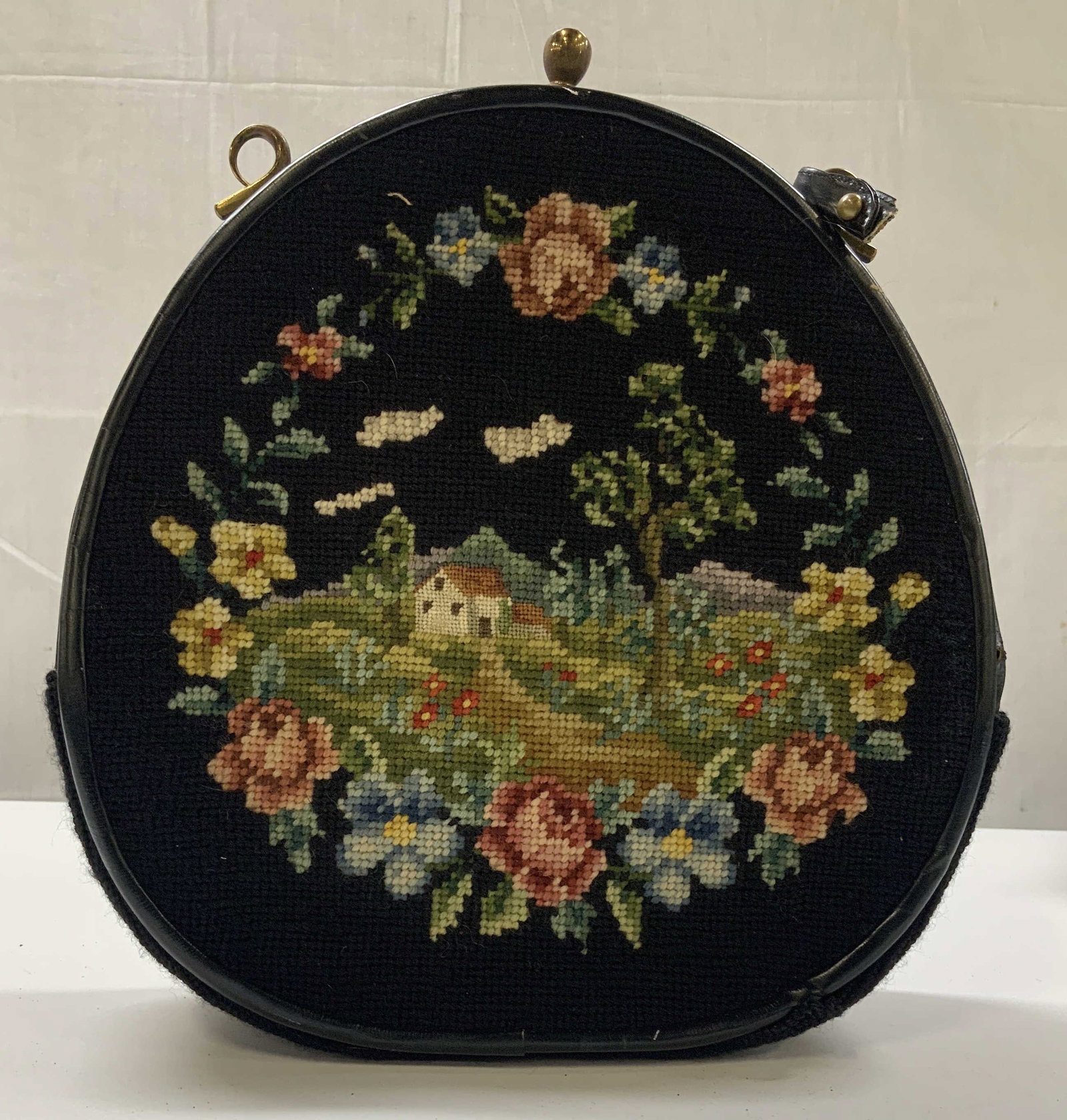 Vntg black needlepoint bag: Vintage black needlepoint bag. Features a detailed pastoral landscape motif framed by a floral wreath. It has a structured round frame known as canteen shape. It has leather piping trim, brass hardwar
