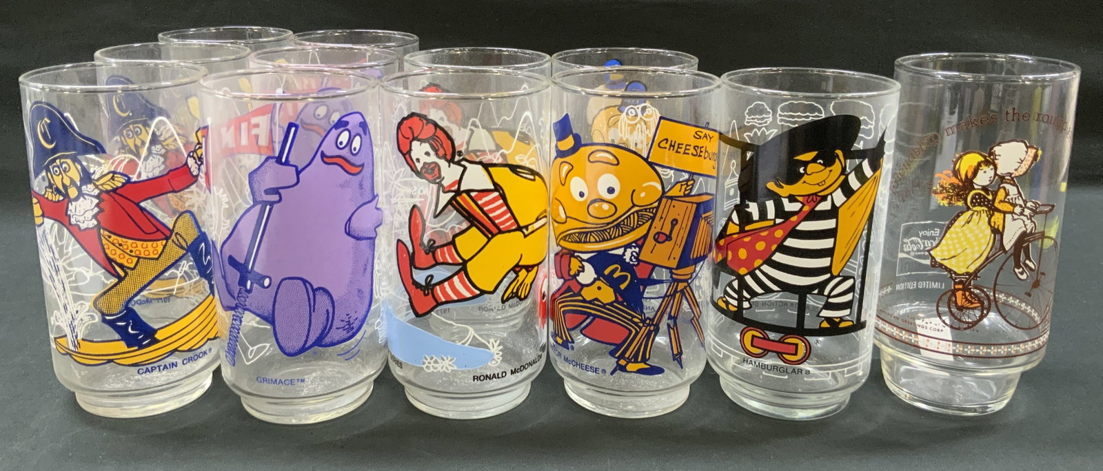 Vtg 1970s Lt12 McDonalds Action Glasses: Vintage 1977 Lot of 11 McDonalds Action series glasses and 1x Holly Hobbie Coca Cola Promo Glass. McDonalds glasses with silkscreened graphic characters like Captain Crook, Grimace, Ronald McDonald, a