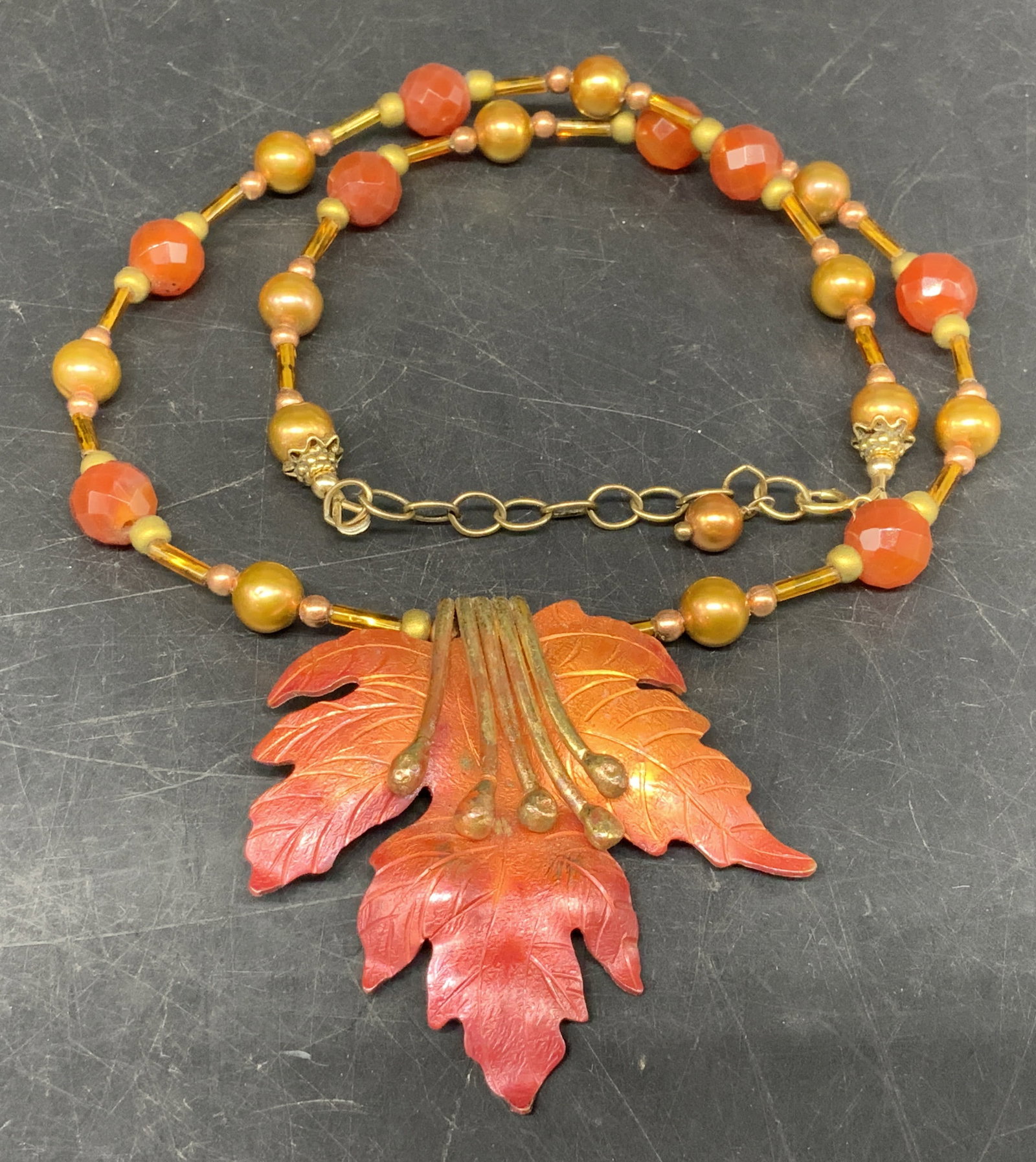 Autumn Leaf Beaded Necklace: Glass Beaded Necklace With Enameled Autumn Leaf Pendant. Pendant is brass-toned metal, possibly gold-filled. Clasp reads 14K Gold-Filled. Orange and gilt round and cylindrical beads. Coating loss pres