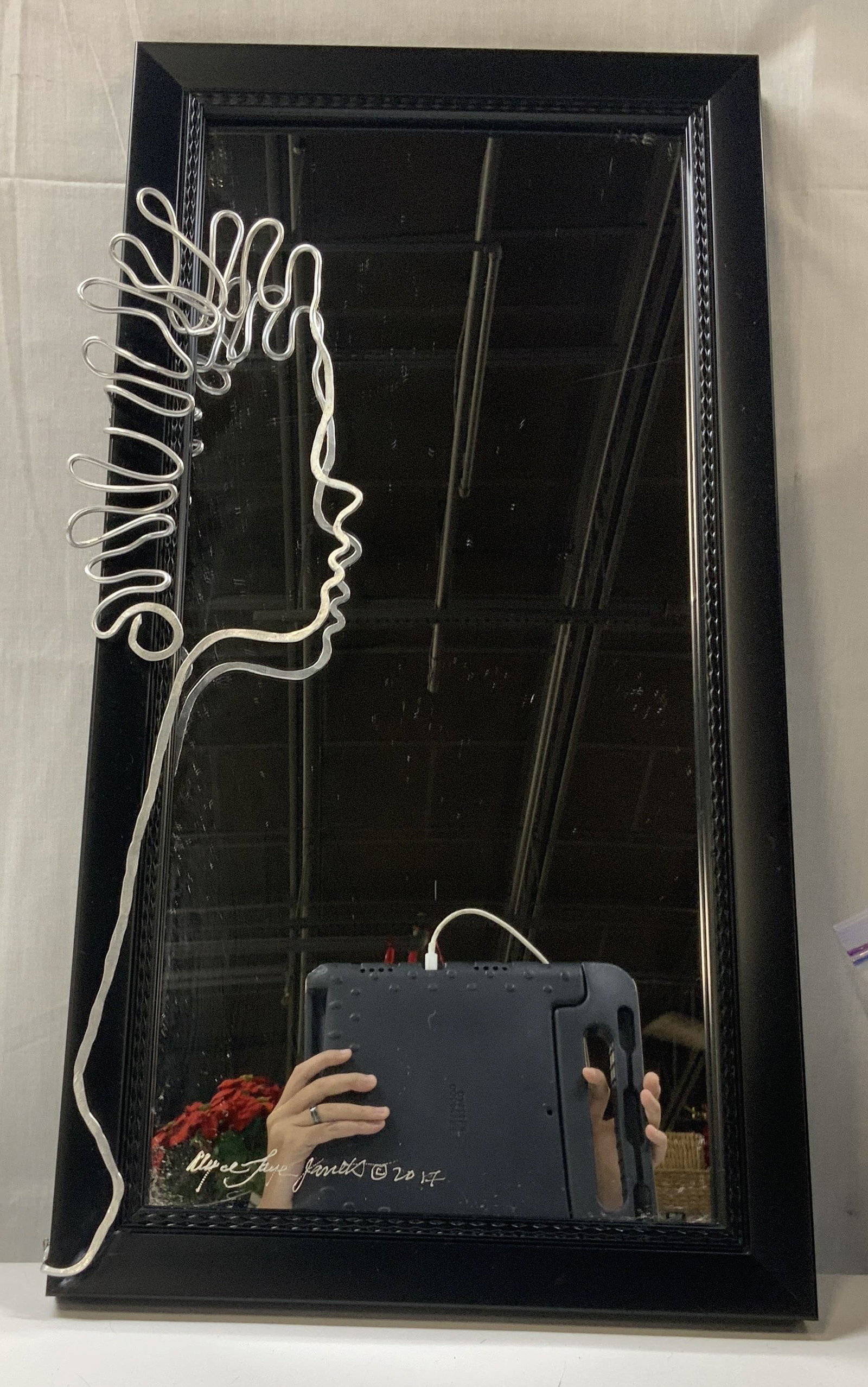 Signed Janet Minimalist wire art mirror 2017: Minimalist wire art mirror. The mirror is a standard rectangular mirror with a black textured frame. The profile of the womens face is created using one line Art using the metal material The artists s
