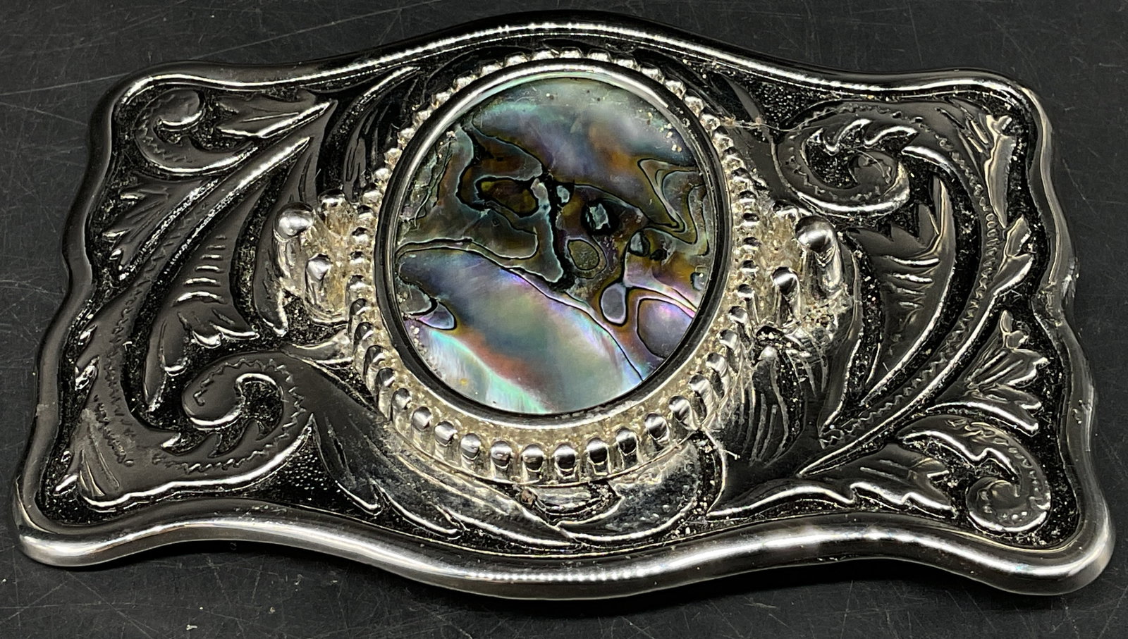 Vtg Western-Style Abalone Shell Belt Buckle: Vintage Western-Style Silver-Toned Belt Buckle. Detailed floral scrollwork engraving. Iridescent swirled abalone shell cabochon center. Condition consistent with age and exposure. Measures app 2in H x