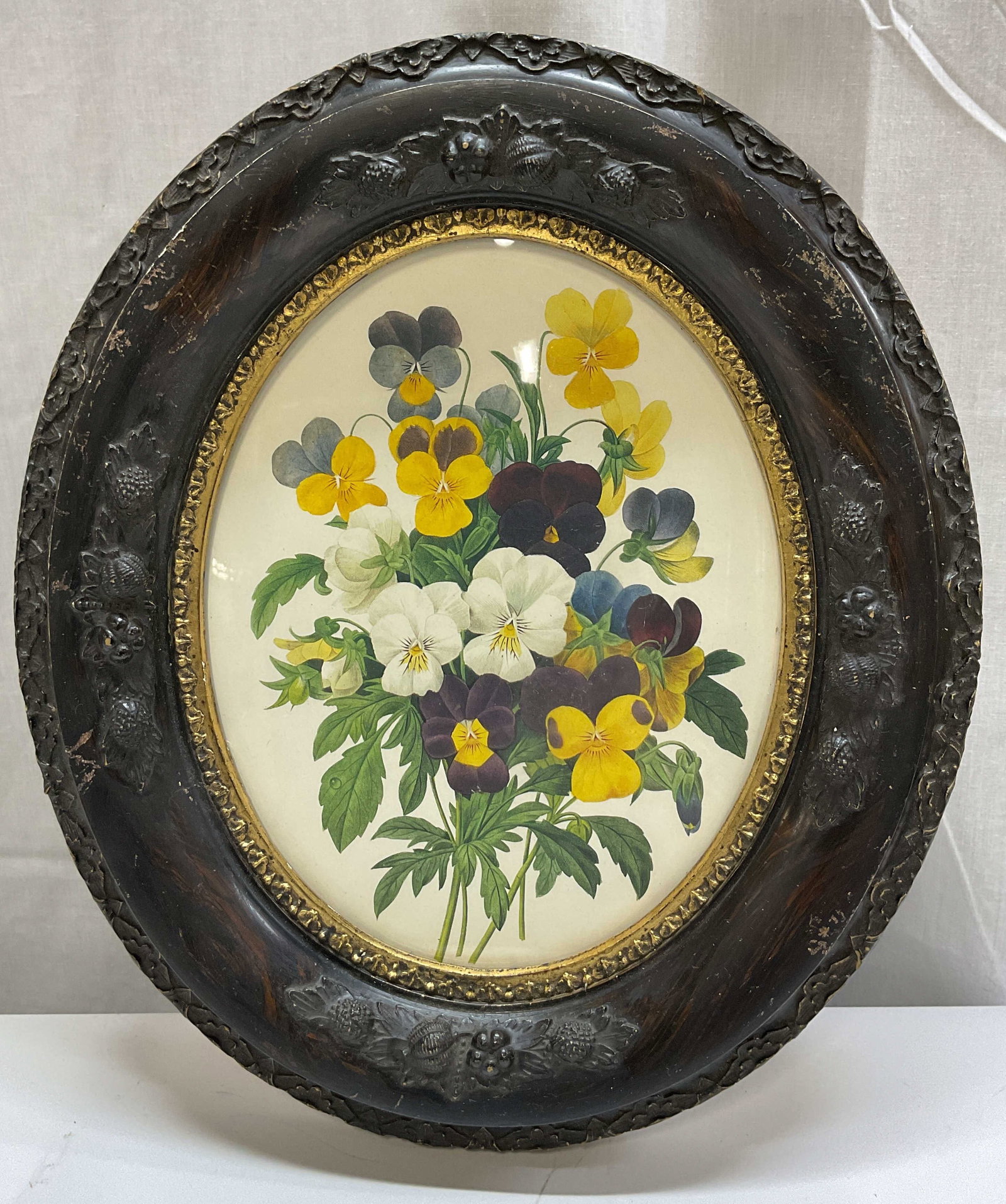 Vintage Oval Framed Botanical Print: Vintage oval framed botanical print. Housed in an oval wooden frame with carved embossed floral motifs. Gilt embossed inner border. Botanical print of floral motifs in varying colors. Measures approx 