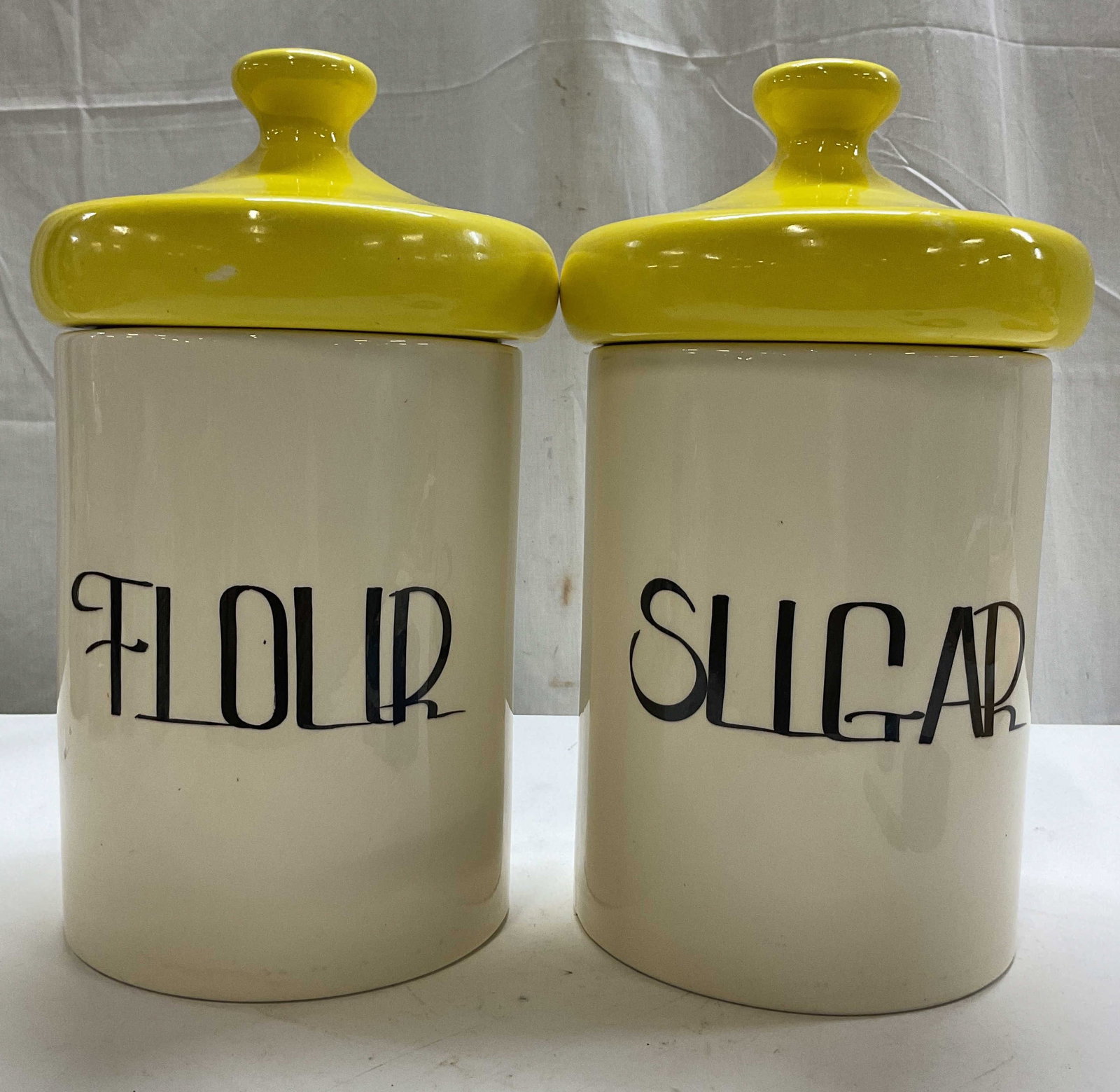 Pair Vintage Mushroom Lid Ceramic Canisters: Pair of vintage mushroom lid ceramic canisters. Yellow mushroom shaped lids with finial. Reads Flour and Sugar. White body with dark text. Glossy finish. Measures ht approx 13 inches diam approx 6.5