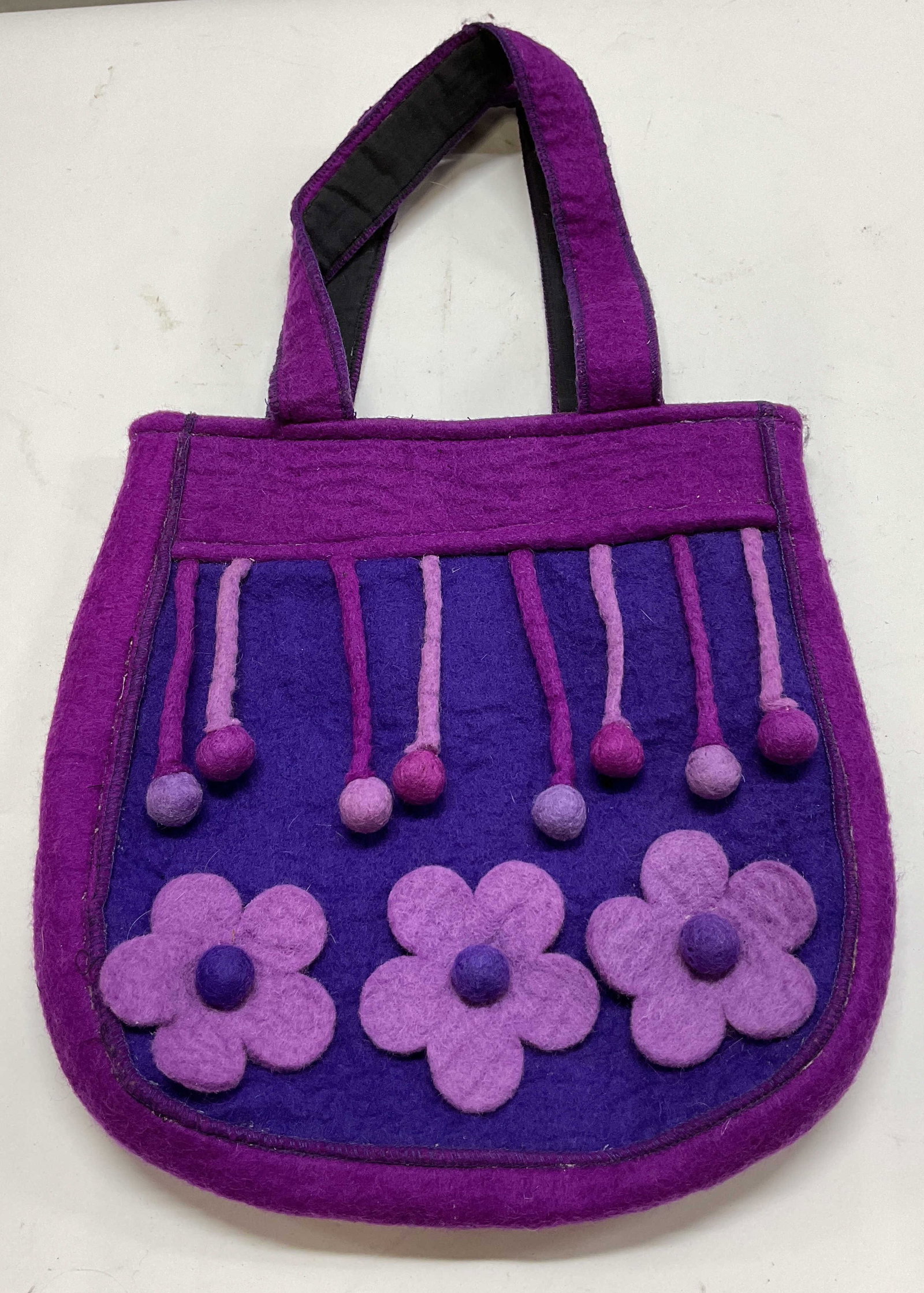 Vintage Purple Wool Floral & Fringed Shoulder Bag: Vintage purple wool floral and fringed shoulder bag. 100% wool. Attached handles. Fringe with pom pom ends. Applied floral motifs. Velcro closure. Interior compartments. Measures approx 12 x 12.5