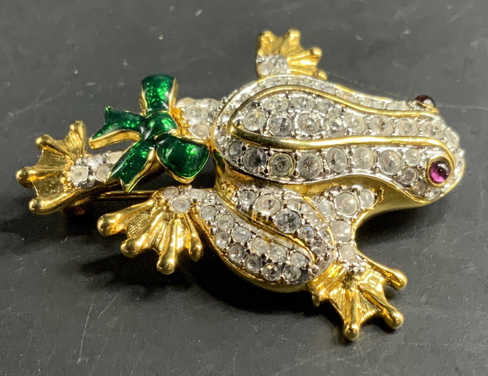 Sgnd KJL rhinestone Crystal Frog Brooch: Signed KJL, Kenneth J Lane Crystal encrusted frog form brooch, red crystal eyes, green enamel bow, gold toned form, measures length app 2 inches, estate jewelry, vintage jewelry, -j