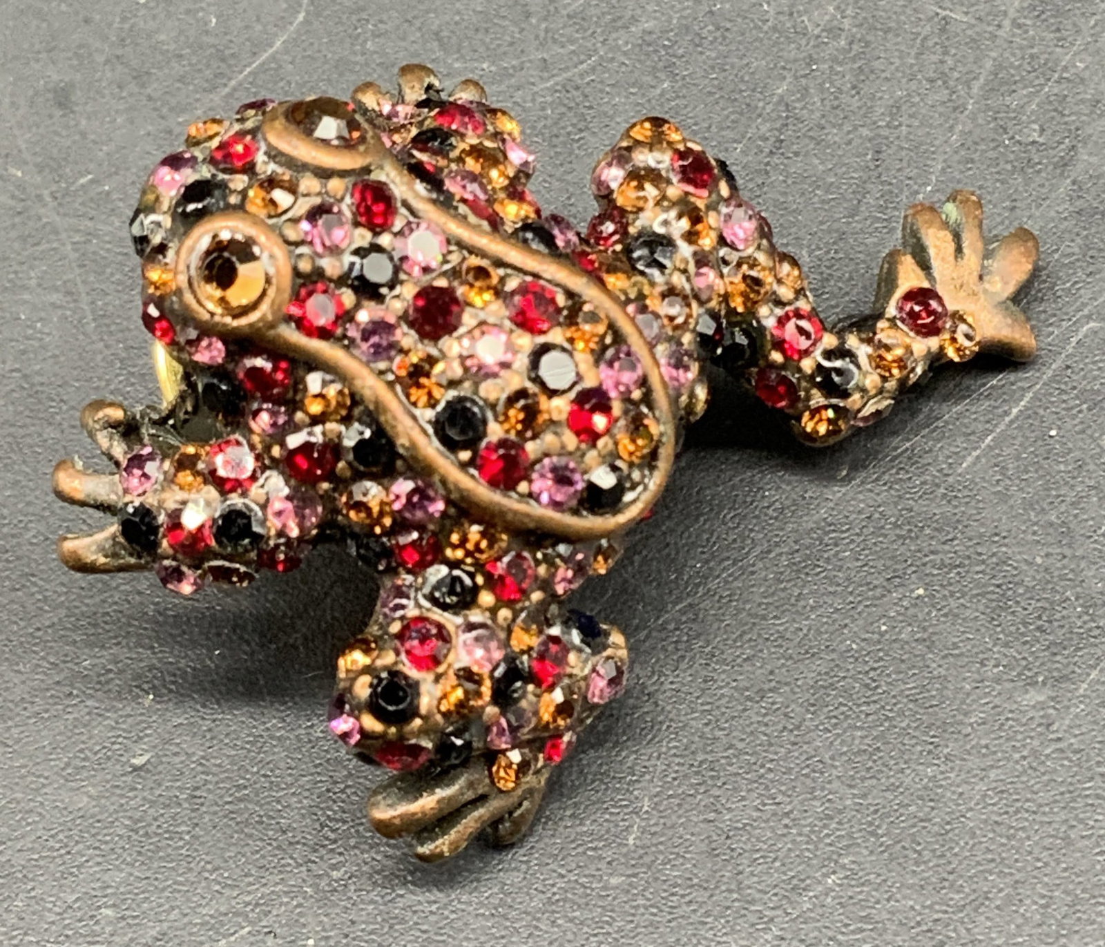 Vntg Chicos Multi colored Rhinestone Frog Brooch: Vintage signed Chicos multi colored Rhinestone Frog brooch, pin, with antique bronze finish, features an encrusted blend of red, pink, orange and black crystals, with larger amber colored eyes, measur