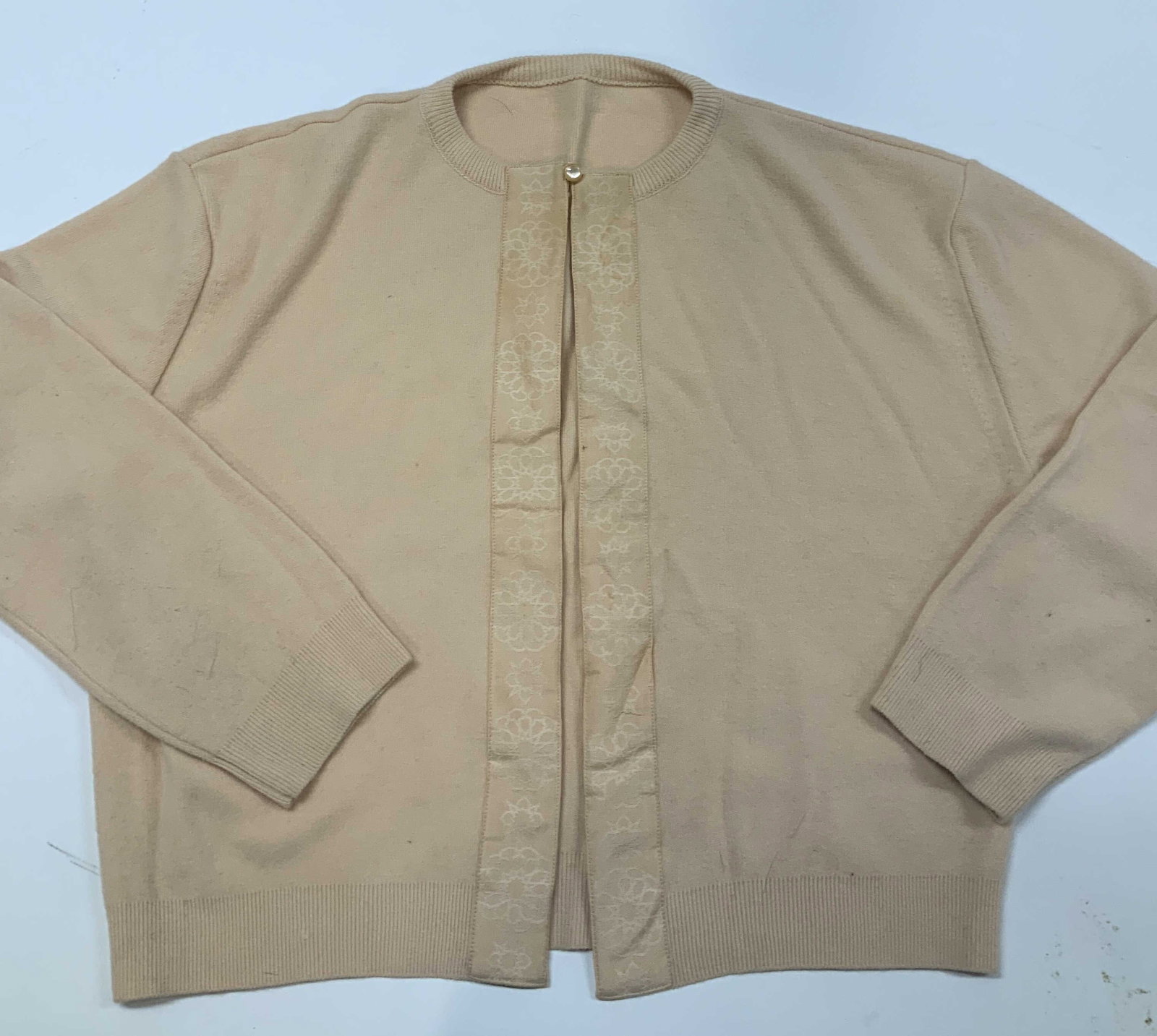 Vntg peach toned knit cardigan.: Vintage peach toned knit cardigan. It has a clean ribbed neckline. It has an open front design with one button at the top. The placate is lined with an elegant embroidered floral trim. Fabric is a ver