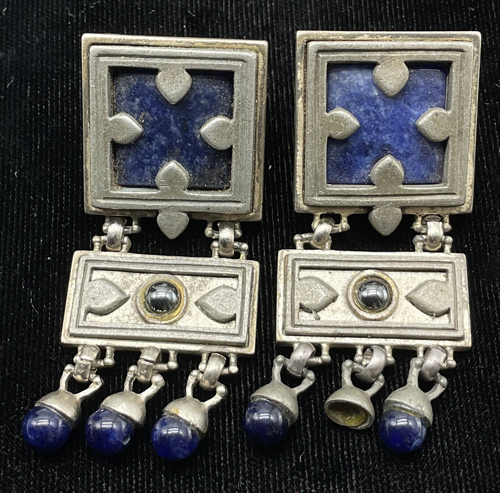 Roxanne Assoulin Blue Dangle Clip On Earrings: Roxanne Assoulin blue silver toned dangle clip on earrings. Backside is marked Roxanne Assoulin. Blue enameled square. Blue semiprecious gemstone dangle design. Measures approx 1 x 2 inches.