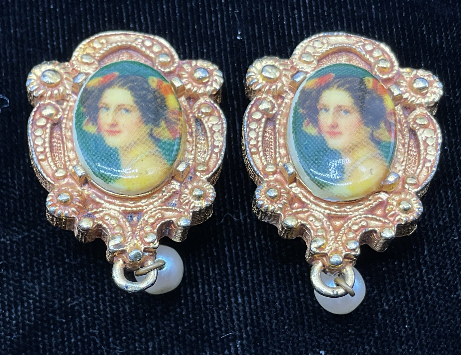 Maeve Carr Cameo Portrait Dangle Clip On Earrings: Maeve Carr cameo porcelain portrait gold toned dangle clip on earrings. Backside is marked Maeve Carr New York. Ornate scroll design. Central portrait of a Victorian lady, painted in varying colors.