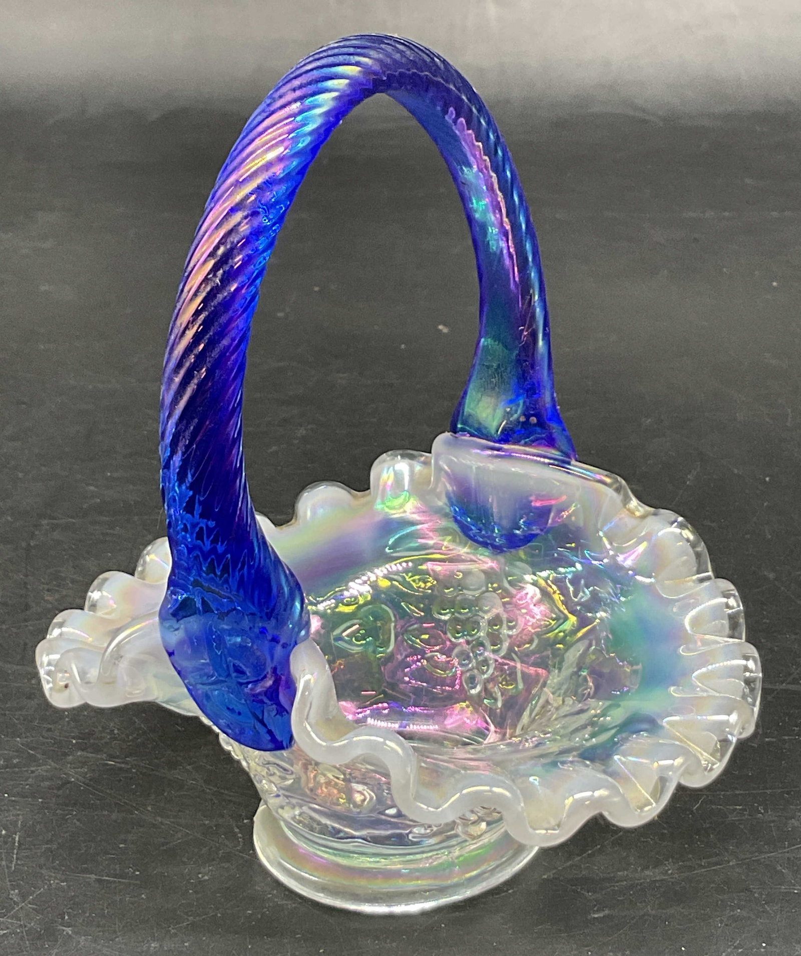 Vtg Fenton Iridescent French Opalescent Basket: Vintage Fenton iridescent iridized French opalescent glass miniature basket. Marked on underside. Cobalt blue twisted handle. Scalloped ruffled edge. Iridescent white with embossed grapevine design. M