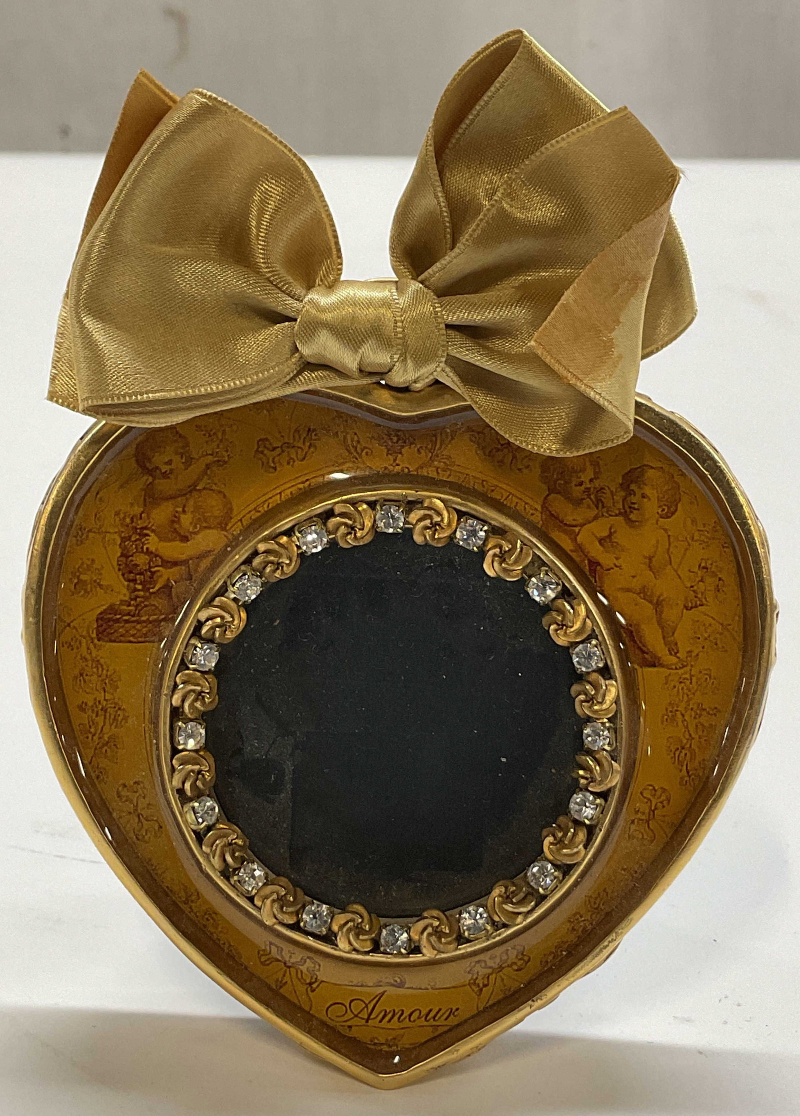John Wind Heart Shaped Bow Picture Frame: John Wind heart shaped bow picture frame. Marked on backside, reads An Original Maximal Art Design By John Wind. Gold toned heart shaped frame with embossed scroll motifs. Gold toned bow at top. Cheru