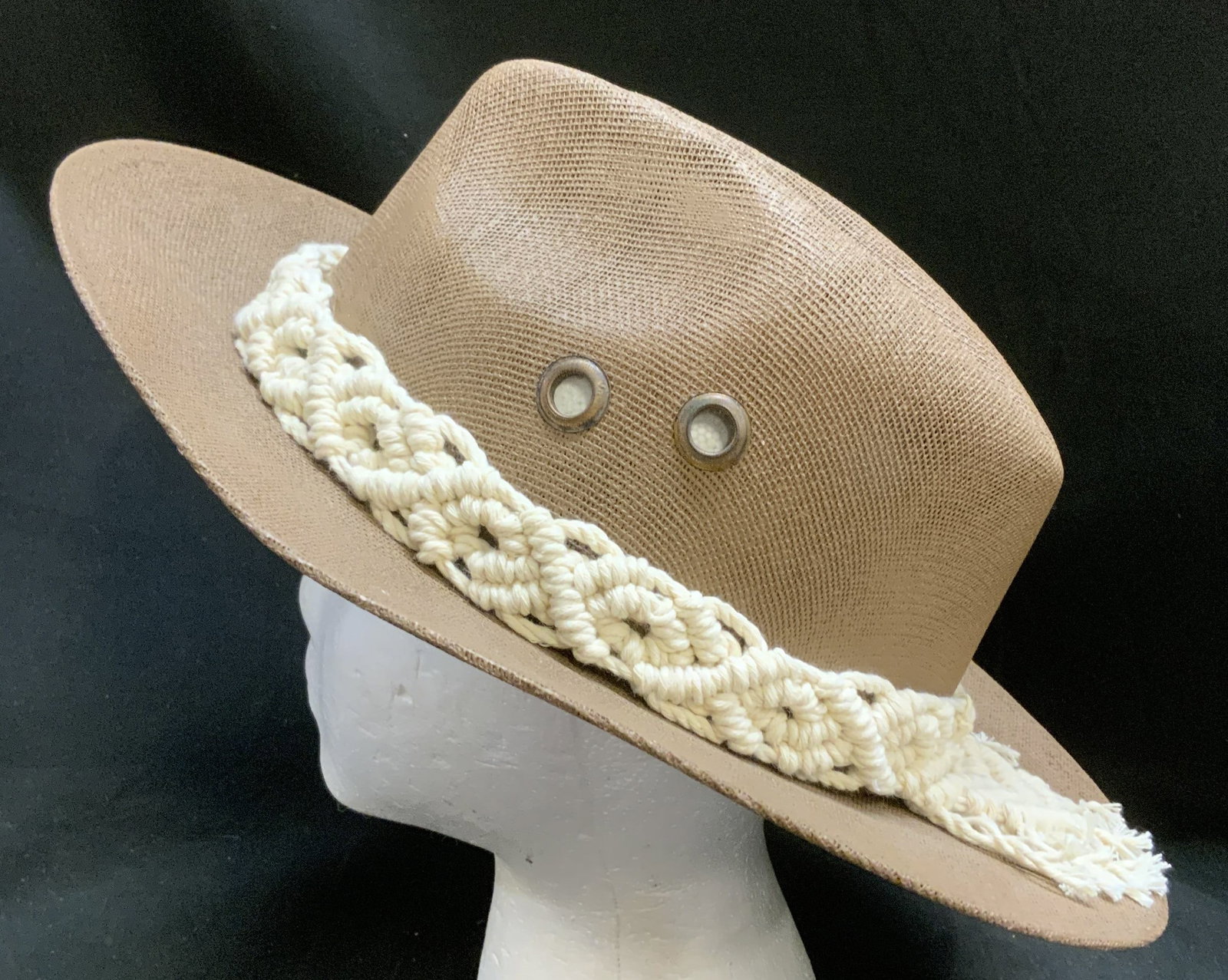 Outback-Style Trail Hat W Macrame Band, Mexico: Brown Outback-Style Trail Hat. Woven mesh material. Two metal grommet ventilation eyelets. Cream colored macrame knotted hat band with fringe at the back. Mexico. Size large. Condition consistent with