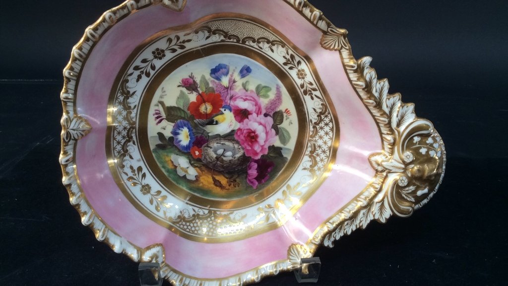 Antique porcelain shaped dish C 1820: a very colorful antique 19th century shaped dish. In the center of this piece there are pink orange blue lavender flowers accompany a bird guarding its nest of eggs. It has a shaped gilt scalloped bor