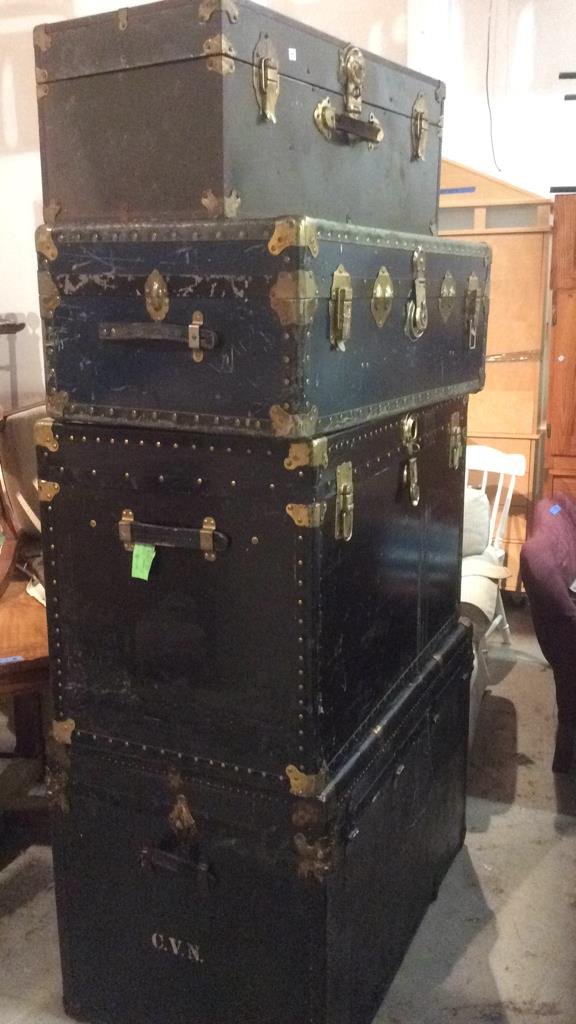 4 Vintage Trunks: Smallest trunk is brown with gold metal accents and 3 clasps for opening and closing and slightly worn handle, measurement in inches 30l x 15w x 12.5h, larger trunk is navy with a black strip, gold me