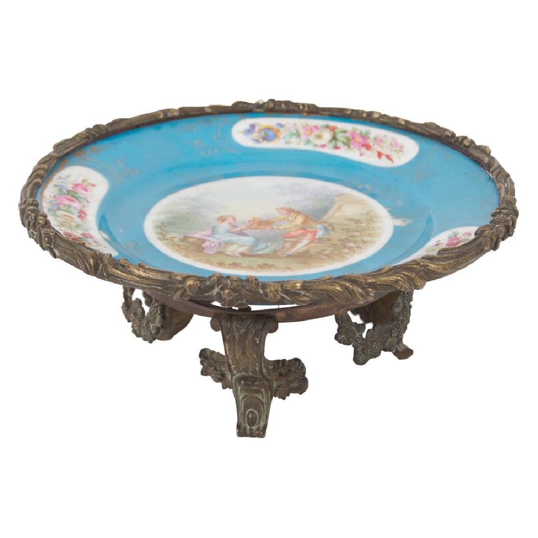 ALZATA in porcellana Ch. de Dreux decorata raffigurante: ALZATA in porcellana Ch. de Dreux decorata raffigurante "Scena galante", base in bronzo (restauro). Francia fine XIX secolo Misure: Diametro cm 25 x h 11