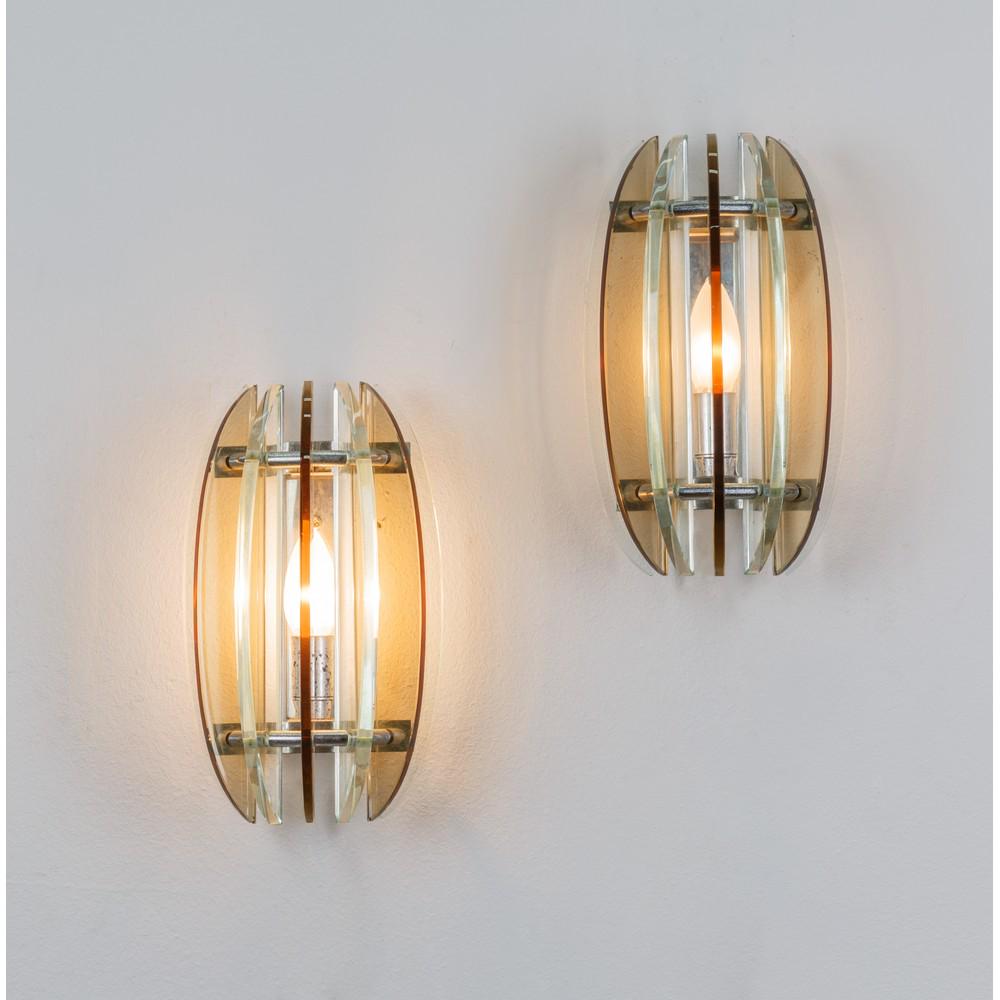 VECA, Coppia di lampade da parete: VECA Produzione Italia 1970 ca. Coppia di lampade da parete ad una luce, corpo ovalizzato in lame di vetro trasparente e ambra, struttura in metallo cromato, etichetta sul fondo. cm 17 x 9 x Alt. 28.