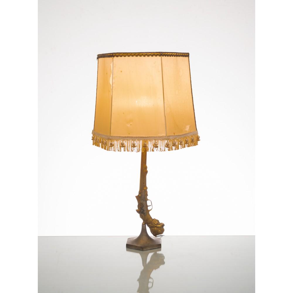 PIETRO FORNASETTI (Attr.le), Lampada da tavolo: PIETRO FORNASETTI (Attr.le) Produzione Italia, 1960 ca. Lampada da tavolo ad una luce, struttura in metallo dorato riproducente una pistola, base esagonale, paralume in tessuto chiaro. cm Alt. 67 . TA