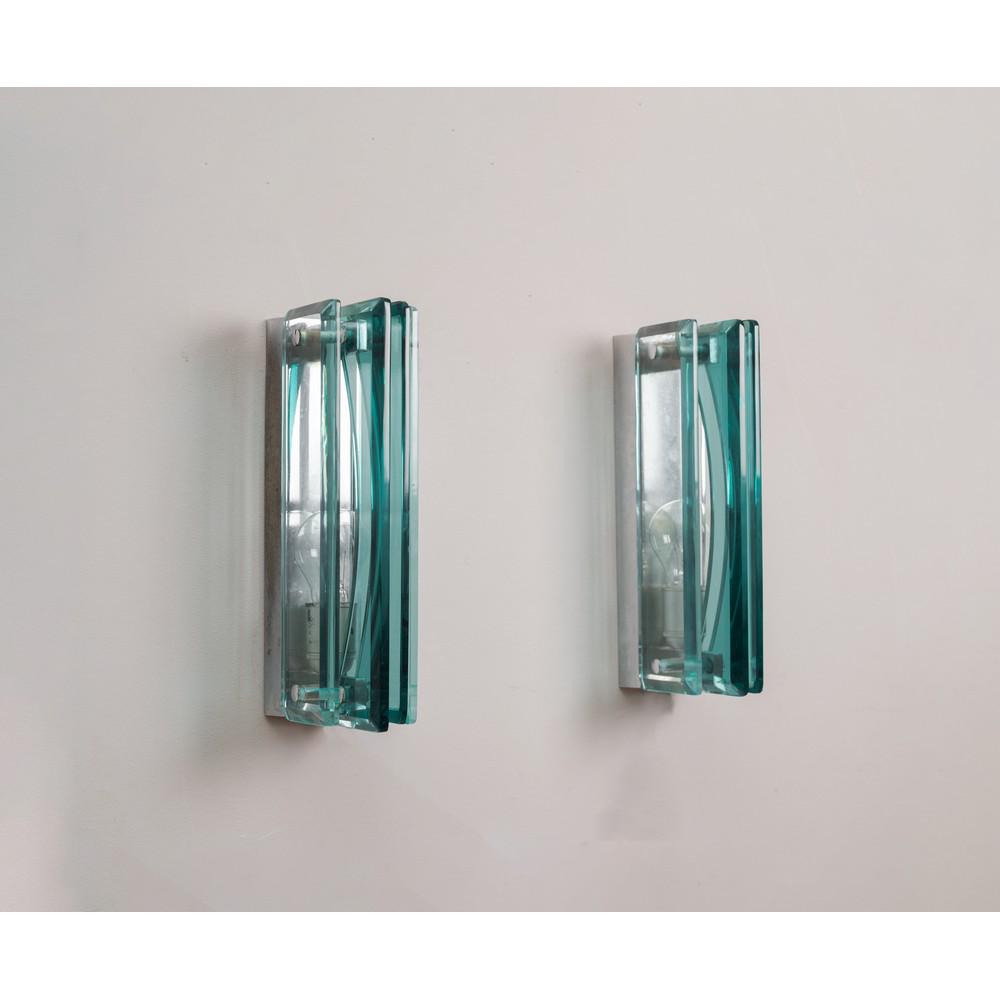 VECA (Attr.le), Coppia di lampade da parete: VECA (Attr.le) Produzione Italia 1960 ca. Coppia di lampade da parete ad una luce in vetro di grosso spessore composte da quattro lastre parallele, struttura in metallo cromato. cm 8 x 15 Alt. 32. PAI