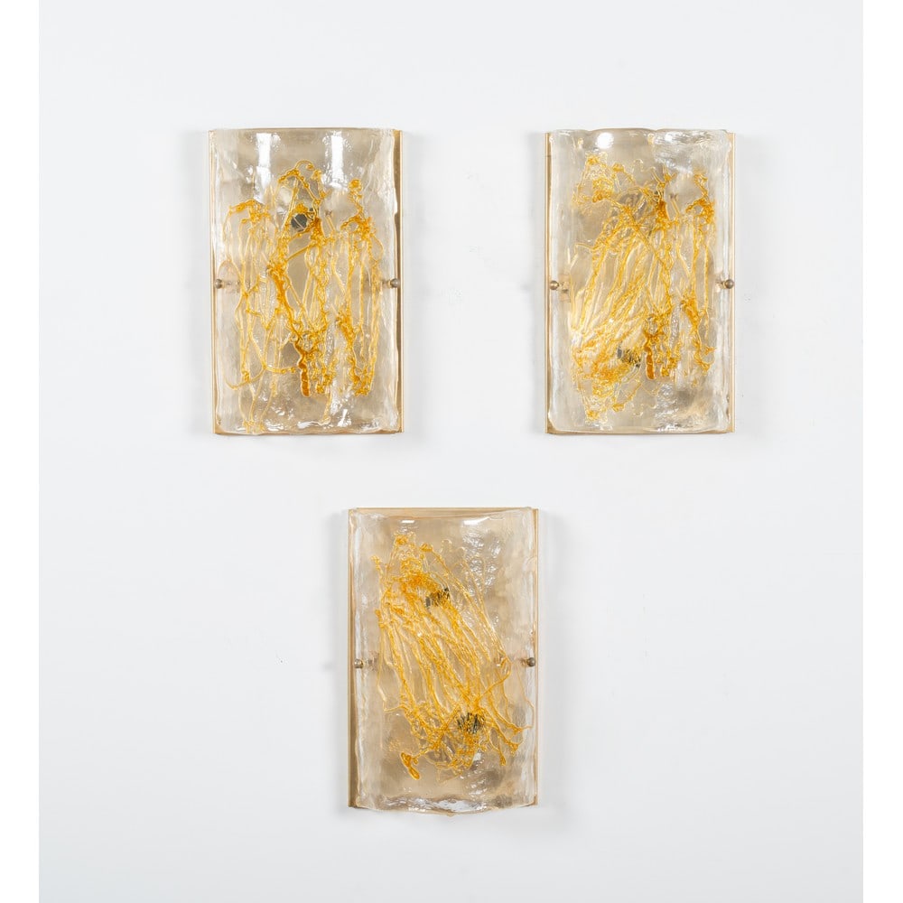 LA MURRINA, Tre lampade da parete: LA MURRINA Produzione Italia 1980 ca. Tre lampade da parete ad una luce, struttura in metallo dorato, diffusore curvato in vetro corteccia decorato con filamenti in vetro ambra. Marchio di produzione.