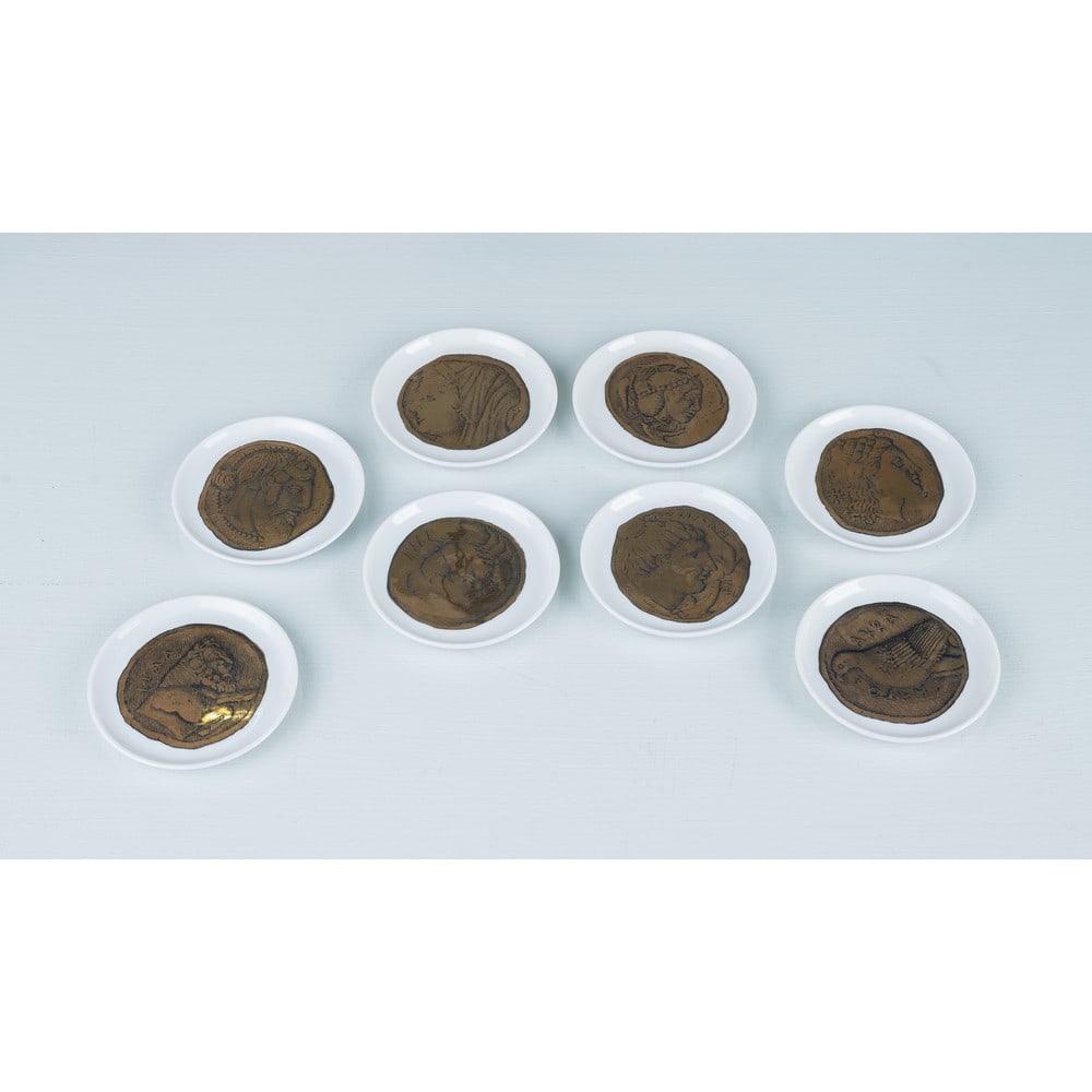 PIERO FORNASETTI, Otto piatti della serie “Monete Romane”: PIERO FORNASETTI Produzione Fornasetti, Italia 1964 ca. Otto piatti della serie “Monete Romane” in ceramica serigrafata in nero e oro raffiguranti antiche monete. Segni di uso. Marchio di