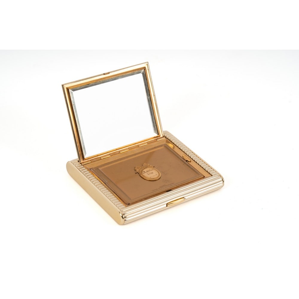CHRISTIAN DIOR, Portacipria in metallo: CHRISTIAN DIOR Produzione Francia 1960 ca. Portacipria in metallo dorato lavorato con listellature orizzontali, apertura a scatto, cristallo specchiato e molato, logo sovrapposto, tampone per cipria. 