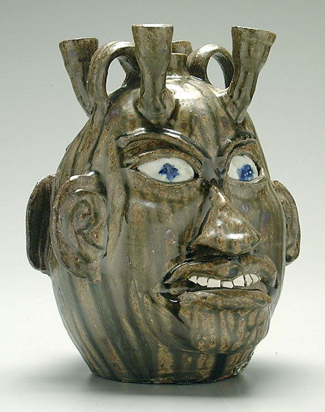 Stoneware double face jug candelabra,: broken china teeth, blue eyes, runny olive alkaline glaze, marked on base "Chester Hewell USA 1998 Last mill of clay Lanier ground", referring to Lanier Meaders, Chester Hewell, 5th generation North G