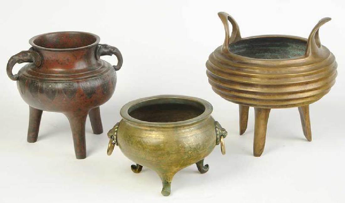 Three Asian Bronze Decorated Censers: Ding form, one with ribbed body and apocryphal reign mark; one with patinated surface and elephant form handles; one with a stipple-decorated body and mask ring handles, 5-1/2 in. to 10-1/2 in. P