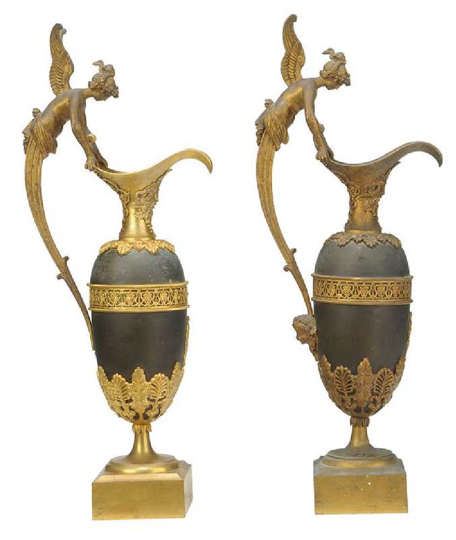 Pair Directoire Ormolu, Patinated Bronze Ewers: French, 19th century, each with ovoid body with winged nymph handle terminating to a cherub mask, spout over foliate masks, applied acanthus leaves and classical figures, resting on a square gilt base
