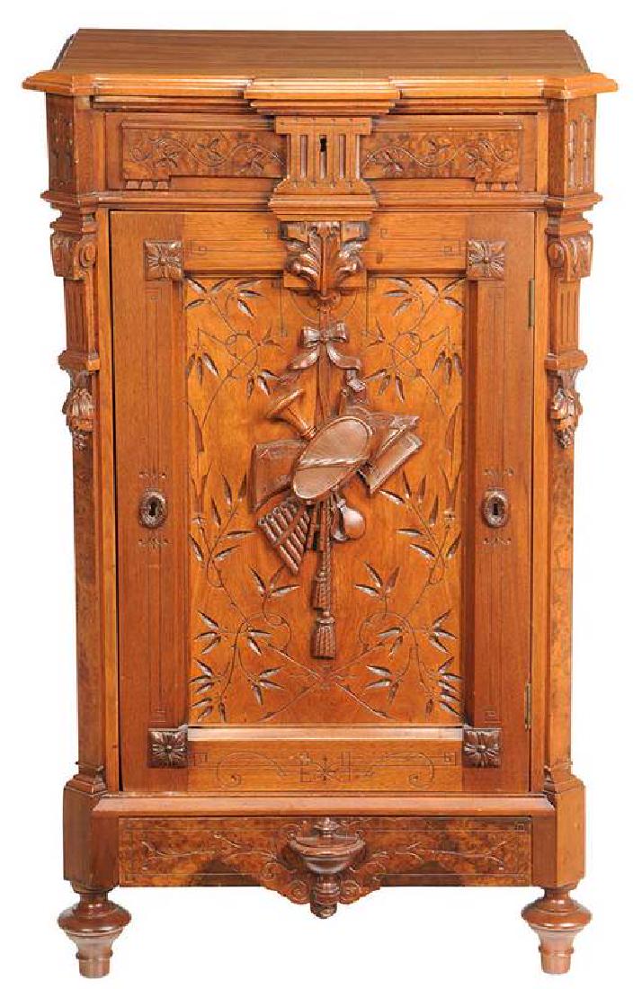 Aesthetic Movement Walnut Music Cabinet: American, late 19th century, burlwood frieze drawer over a cabinet door with carved musical trophy, open interior, over a base drawer, 40-3/4 x 25 x 18 in. Provenance: Property From an Important Tenne