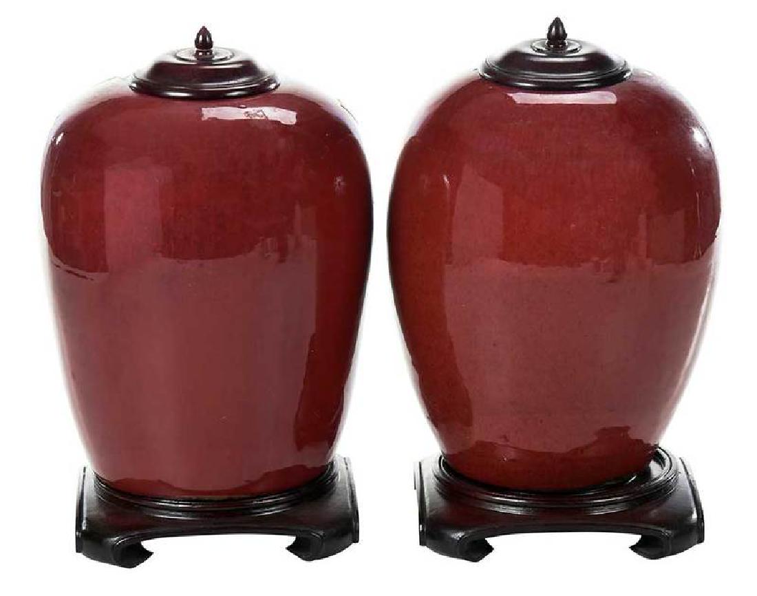 Near Pair Chinese Sang de Boeuf Jars on Stands: Republic period or earlier, each with associated turned wood lid and carved base, 13-1/2 x 8-1/2 in. Provenance: Private Collection