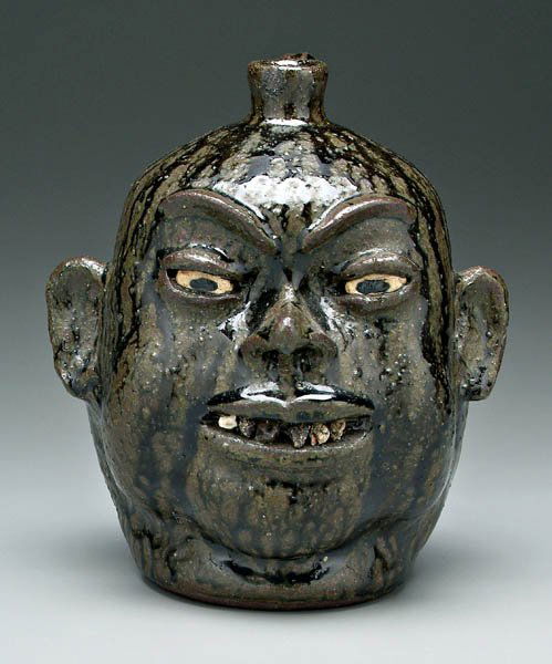 Lanier Meaders stoneware face jug: (1917-1998), broken china teeth of varying colors, runny dark olive alkaline glaze, base signed in script "Lanier Meaders" (White County, Georgia, 1917-1998), 10 in. 1/2 in. shallow rim chip. Provenan