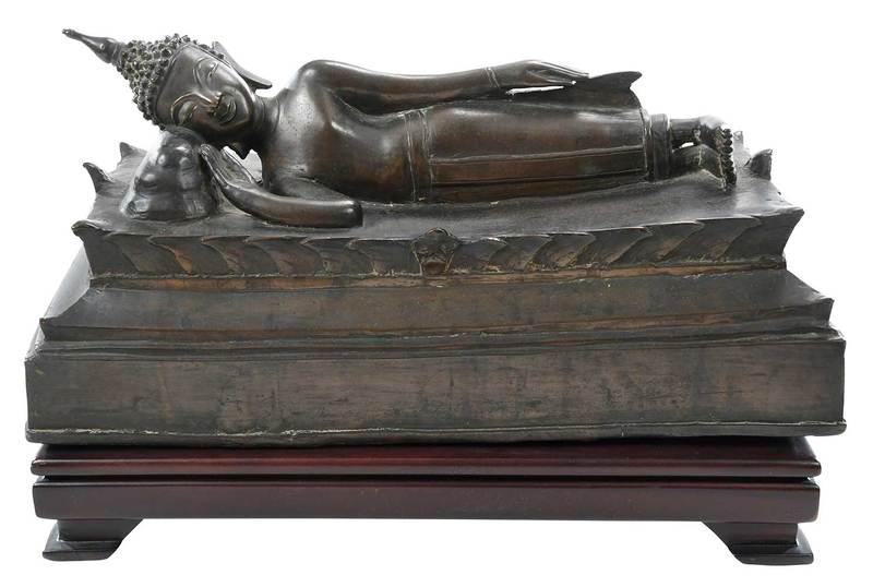 Bronze Figure of Reclining Buddha: Thailand, 19th century, representing Parinirvana, lying on his right side on a stepped and waisted dais, his head resting on a pillow, right arm at an angle, left arm along his body, 6-3/4 x 14-3/4 x 