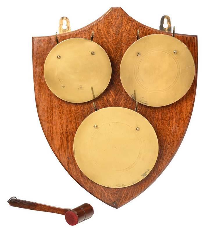Brass and Mahogany Wall Gong: probably American, 20th century, shield shaped mahogany wall plaque with three mounted round brass gongs, carved wood mallet with felt covered ends hang from hook at bottom, 22 in.; Provenance: Privat