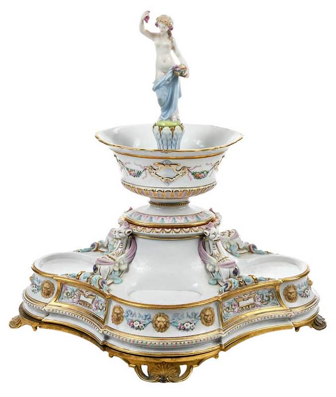 Fine German Three Tiered Figural Centerpiece: late 19th/early 20th century, bronze mounted andÿ hand painted porcelain base with reclining griffins and applied lion masks under floral draped bowl surmounted by draped woman holding basket of grap