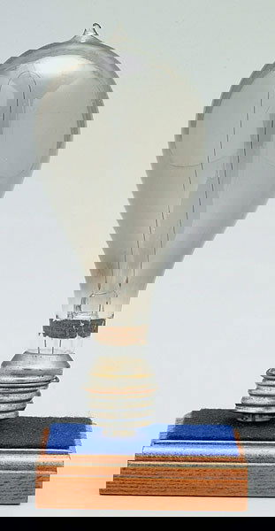 Early Edison light bulb,: mounted on wood block, original paper label "New Type Edison Lamp…Patented 1880", 6 x 2-7/8 in. Chip to tip of bulb, small gap or break in the filament.