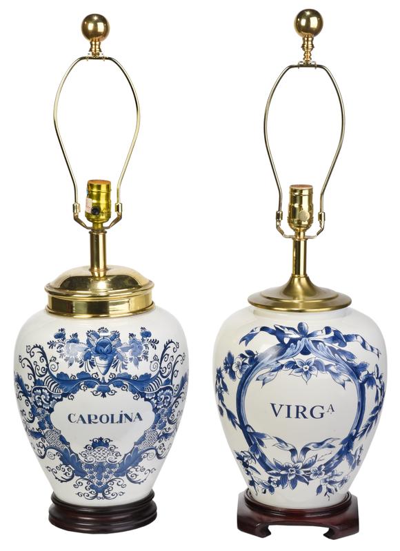 Pair of Blue and White Tobacco Lamps: modern, pair blue and white Delft style, one labeled "Carolina" and one "Viga" within floral cartouches, wood bases, with brass harps and red shades, 19 in. to top of socket, Provenance: Collection of