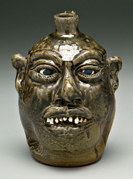 Lanier Meaders stoneware face jug,: ceramic teeth, runny dark olive glaze, base signed "Lanier Meaders" (White County, Georgia, 1917-1998), 9-1/2 in. Excellent condition. Provenance: Private Collection, Jewell, Georgia