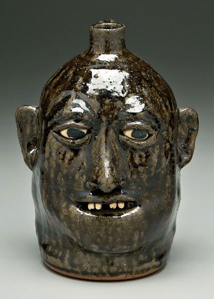 Lanier Meaders stoneware face jug,: ceramic teeth, runny dark olive glaze, base marked "Lanier Meaders" (White County, Georgia, 1917-1998), 10 in. Excellent condition. Provenance: Private Collection, Jewell, Georgia