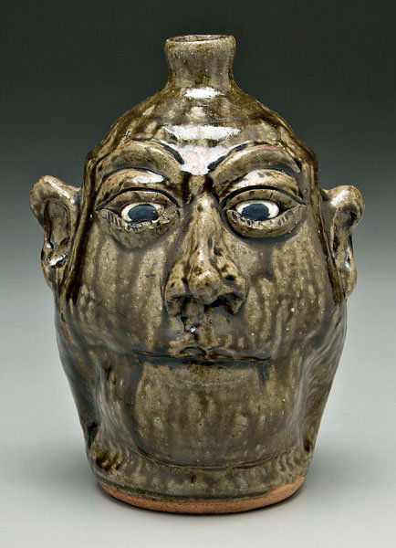Lanier Meaders stoneware face jug,: runny olive glaze, pinched mouth with no teeth, signed on base, "Lanier Meaders" (White County, Georgia, 1917-1998), 10 in. Excellent condition. Provenance: Collection of Merrill and Ethelda Oxley