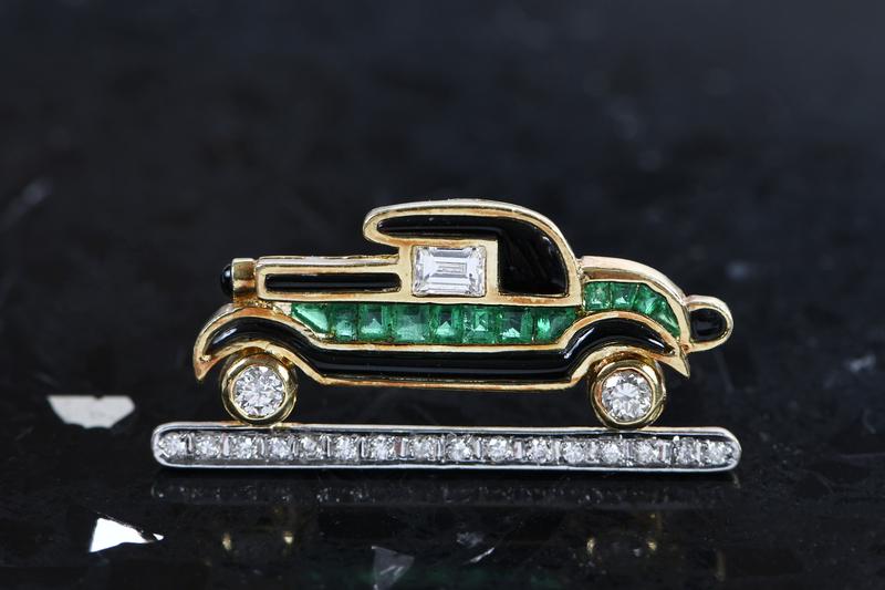 18kt. Gemstone Roadster Brooch: assorted cut diamonds estimated total weight 0.50ct., calibre cut emeralds and black onyx, black enamel, stamped "J.T, 750", yellow gold, 9/16 x 1-1/4 in., 4.9 grams, with appraisalProvenance: The Mil