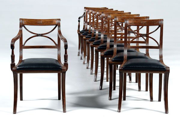 Set of ten Duncan Phyfe style chairs: comprising two arm and eight side, klismos form, mahogany throughout, each with fascia carved and scrolled crest, all with probably original black leather upholstered slip seats, probably late 19th ce