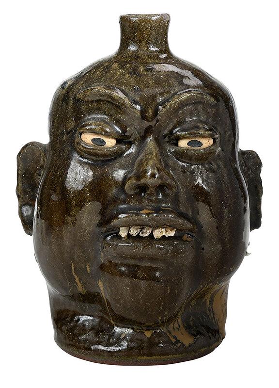 Lanier Meaders Face Jug: (White County, Georgia, 1917-1998) runny green alkaline glaze with brown streaking, applied facial features, white clay eyes, rock teeth, applied strap handle, "Lanier Meaders" inscribed to base, 10-1