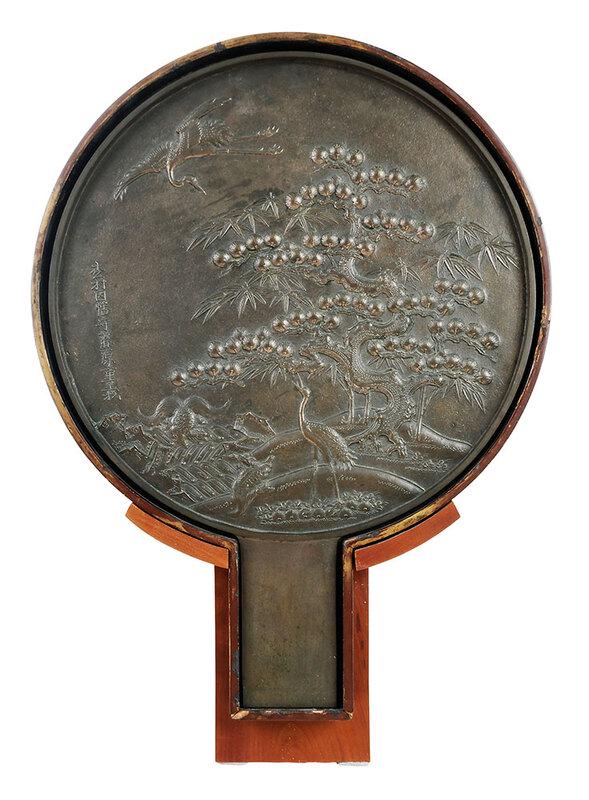 Japanese Cast Bronze Mirror with Stand: probably Meiji period, large bronze hand mirror with circular scene of cranes in a landscape, calligraphic marks to left, rectangular handle, in a fitted lacquer box, with later wood stand, mirror inc