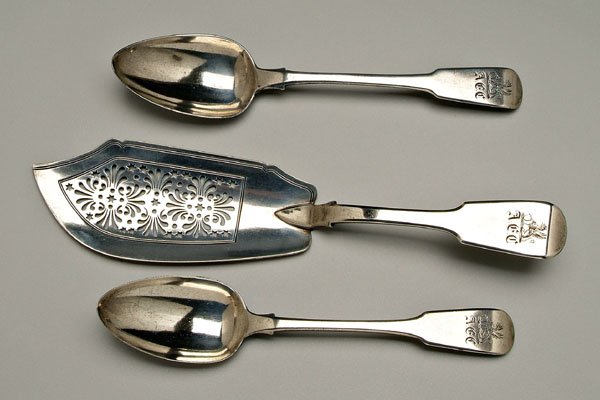 Three pieces English silver flatware,: fiddle handles, marks for William Eaton, London: fish slice, openwork blade, 1828, 11-1/2 in.; two serving spoons, 1802 and 1826, 8-3/4 in., [tip wear,] heraldic device and "A.G.C.". Provenance: Flori